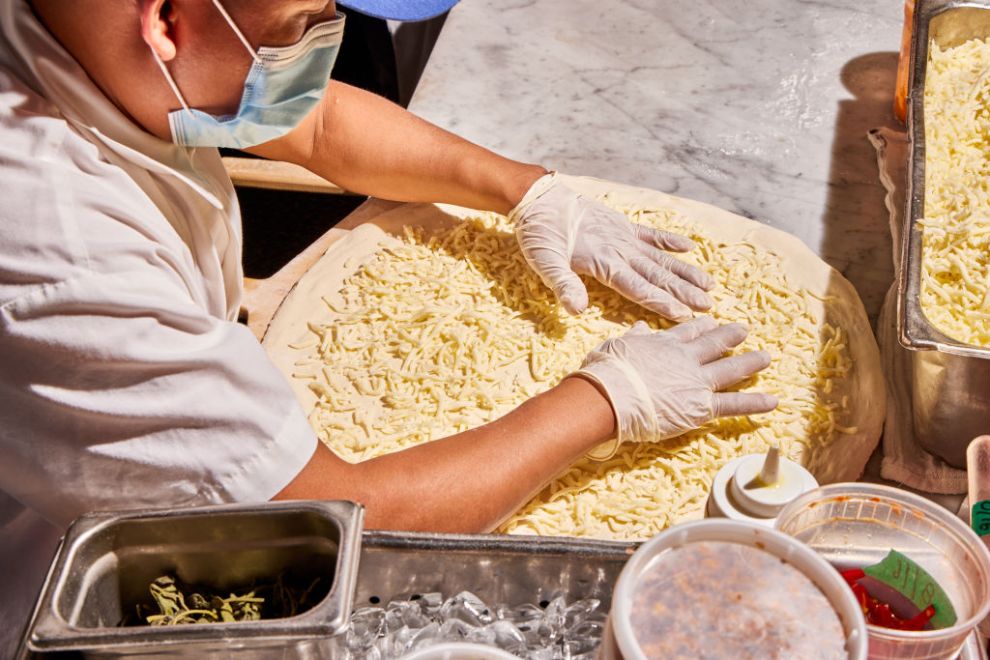 Pizza Maker Brigido De Los Santos Flores preps a cheese pie for the oven at F&F Pizzeria in Brooklyn, NY.